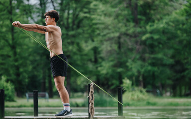 Athletic young man working out with a resistance band in a natural outdoor setting, focusing on...