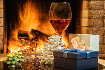 Glass of red wine, candles and Christmas decoration lantern before fireplace.