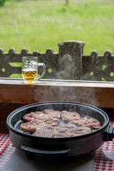 Frying or stewing pork, beef, veal in a special pan. Summer kitchen in the countryside. In the background you can see a mug of beer and a beautiful view of the meadow and the forest.