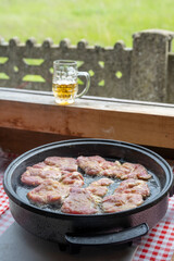 Frying or stewing pork, beef, veal in a special pan. Summer kitchen in the countryside. In the background you can see a mug of beer and a beautiful view of the meadow and the forest.
