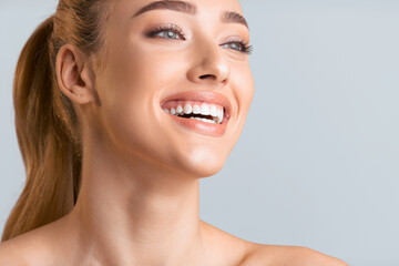 A close-up portrait of a young woman with light brown hair pulled back in a ponytail, smiling brightly. Her skin is fair and glowing, and her teeth are white and bright, copy space