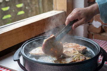 Summer kitchen in the countryside. A man's hand turns pork or beef in a large special pan for frying and stewing meat.