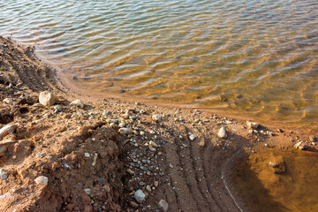 Sandy and rocky shore of a reservoir washed by clear water