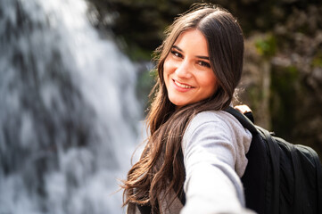 Close-up portrait of a beautiful young woman smiling happily to the camera with a blurred waterfall in the background.