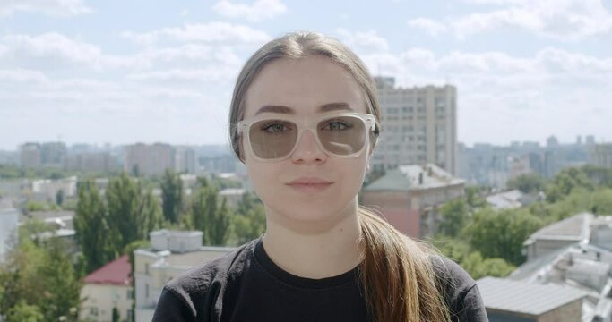Girl wearing glasses with photochromic lenses. The lenses adjust to changing light conditions, becoming darker in the sun after being transparent indoors. Portrait. Urban city landscape background