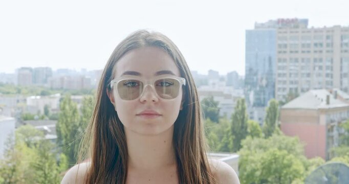 Girl wearing glasses with photochromic lenses. The lenses adjust to changing light conditions, becoming darker in the sun after being transparent indoors. Portrait. Urban city landscape background