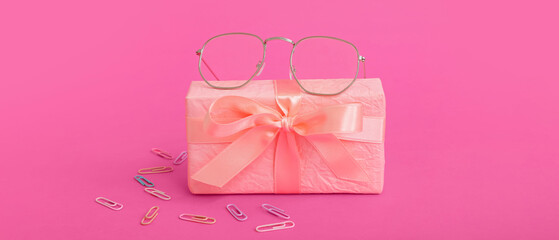 Gift box with eyeglasses and paper clips on pink background
