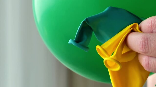 green balloon is inflated and green and yellow balloons in hand on blurry room background.Festive paraphernalia and decorations. 4k footage