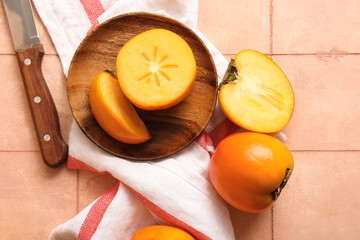 Wooden plate with sweet ripe persimmons on pink tile background