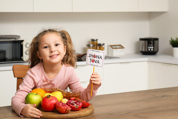 Cute little girl with ripe fruits, honey and Shana Tova greeting card in kitchen. Rosh Hashanah (Jewish New Year) celebration