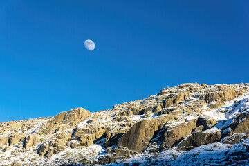 Nice view of the moon over the rocks of a snowy mountain in Avila, Spain