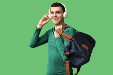 Young man with sports bag and headphones on green background