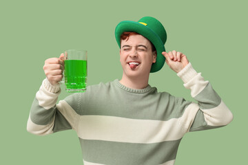 Funny young man in leprechaun's hat with mug of beer on green background. St. Patrick's Day...