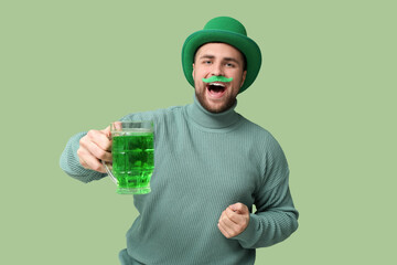 Happy young man with leprechaun's hat and mug of beer on green background. St. Patrick's Day...