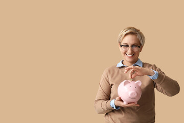 Beautiful mature woman putting coin into pink piggy bank on brown background © Pixel-Shot