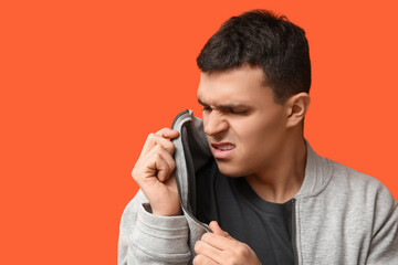 Handsome young man feeling bad smell from dirty clothes on orange background