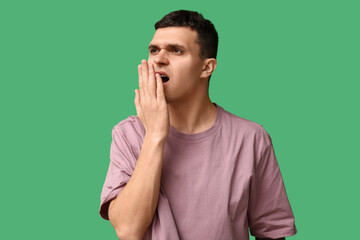 Handsome young man feeling bad smell from mouth on green background