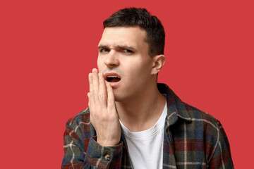Handsome young man feeling bad smell from mouth on red background