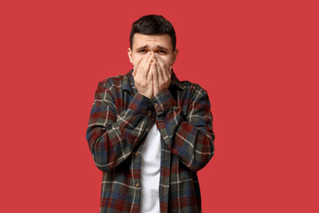 Handsome young man feeling bad smell on red background