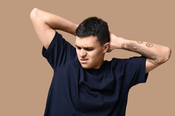Handsome young man feeling bad smell from armpits on beige background