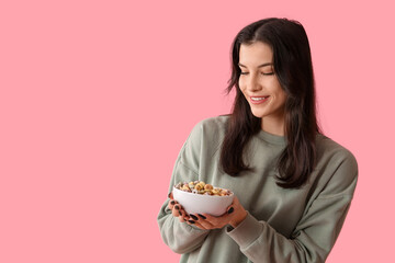 Young woman with bowl of tasty cereal rings on pink background