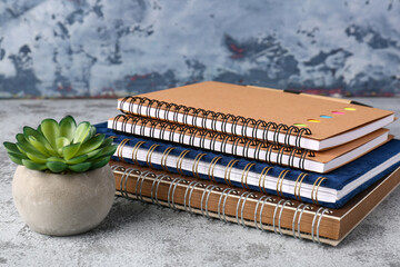 Naklejka premium Stack of notebooks and flower in pot on grunge table near grey wall