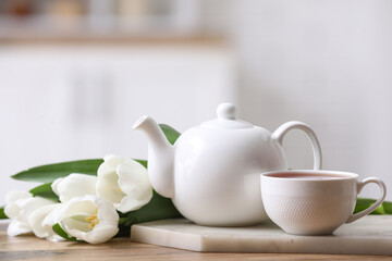 Tea pot and cup near tulips on table against blurred background