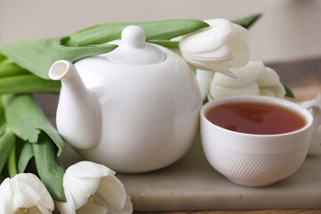 Tea pot and cup near tulips on table against blurred background