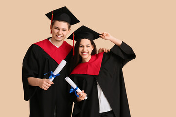 Happy graduate couple with diplomas on beige background