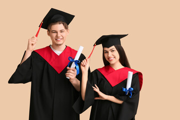 Happy graduate couple with diplomas on beige background
