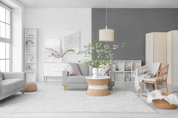 Cozy sofa, chair with plaid and blooming branches in living room
