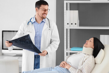 Fototapeta premium Male doctor studying x-ray image of spine with injured woman in clinic