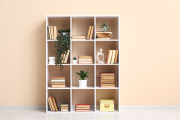 Modern shelving unit with books and home decor near beige wall