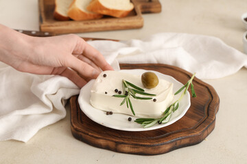 Female hand with plate of tasty feta cheese, olive, rosemary and peppercorn on white background