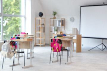 Blurred view of light classroom with projector screen and desks