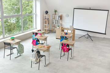 Interior of light classroom with projector screen and desks