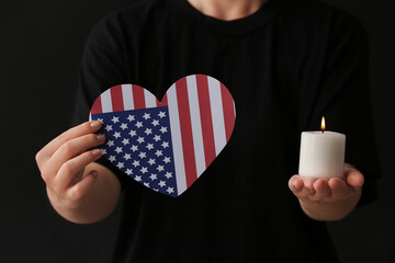 Woman holding burning candle and flag of USA in shape of heart on dark background, closeup....