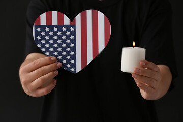 Woman holding burning candle and flag of USA in shape of heart on dark background, closeup....