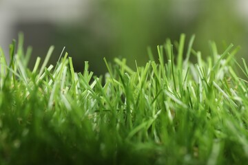 Green artificial grass against blurred background, closeup