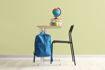 Desk with globe, books and apple near green wall