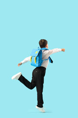 Little schoolboy with backpack jumping on blue background, back view