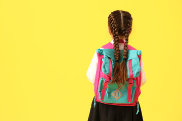 Little schoolgirl with backpack on yellow background, back view