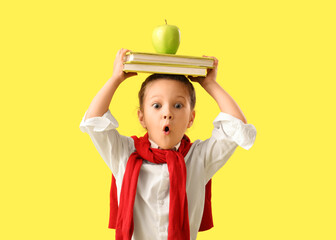 Shocked little schoolgirl with apple and books on yellow background