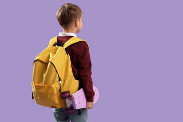 Little schoolboy with yellow backpack and skateboard on lilac background, back view