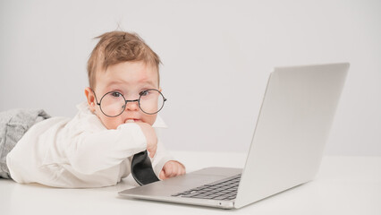 Cute baby in glasses and suit working on laptop. 