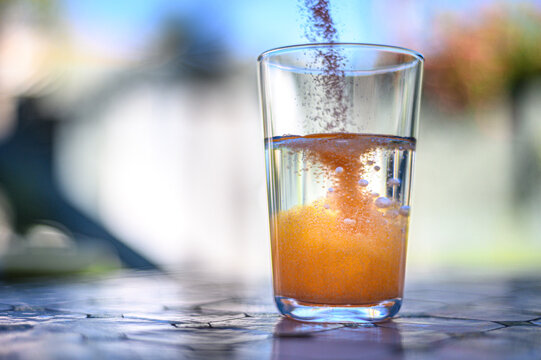 Orange cold paracetamol and salicylamid powder getting poured into a glass of water and dissolving in it with bubbles going up