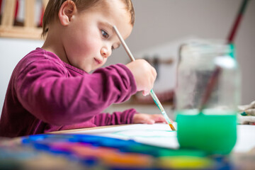 Toodler painting with watercolors on a table with all the tools for the painting workshop.
