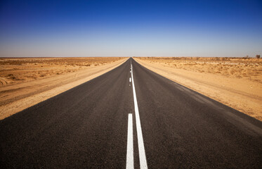 Empty open outback road in South Australia. Straight single-lane asphalt road stretching into the distance. Desert scene with a pure blue cloudless sky. Endless travel and adventure.