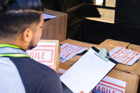 Colombian Latino shipping company worker in his 30s checks the destination list of parcels