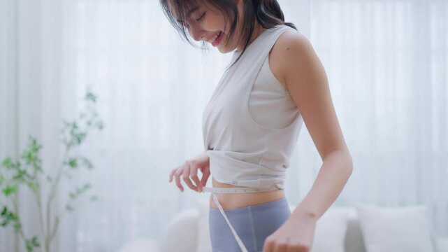 Young Asian woman in sportswear measuring her waist with a tape. Diet and healthy concept. Body shape slim